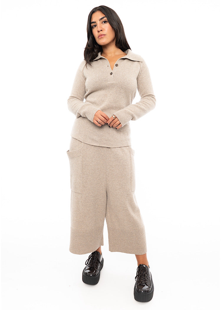 A Full Frame photo of A Model wearing a beige Pullover, featuring a V-neckline, buttons and a ribbed cuff. Paired with A Matching Trouser and patent shoe.