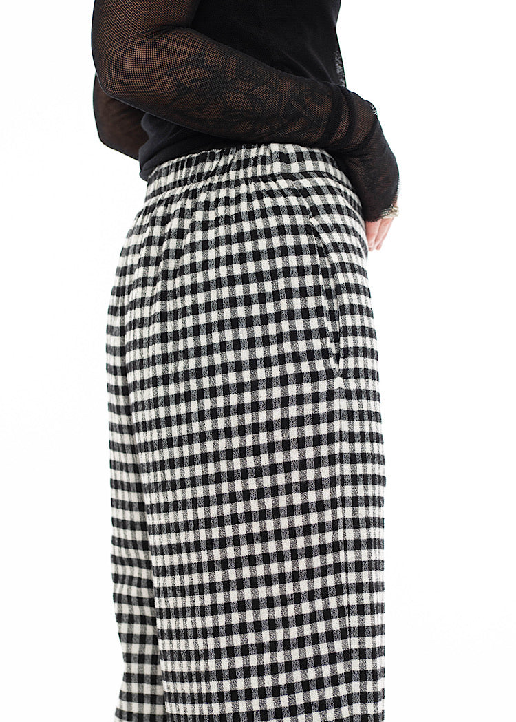 Close up of model wearing black and white gingham check wide-leg trousers with side pockets and elasticated rear waistband, styled with mesh black top.