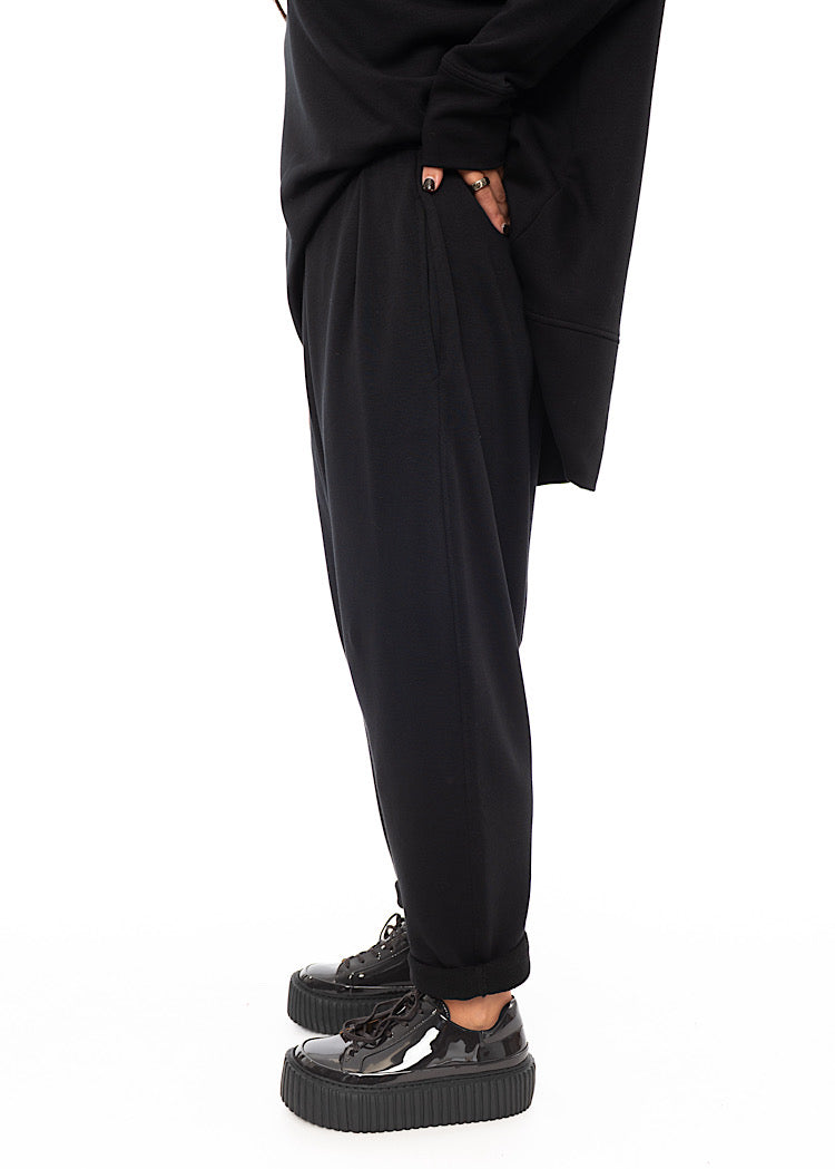 A Model standing to a side wearing a Black fitted Trouser with a semi rolled up ankle. Showing the Trousers fit.