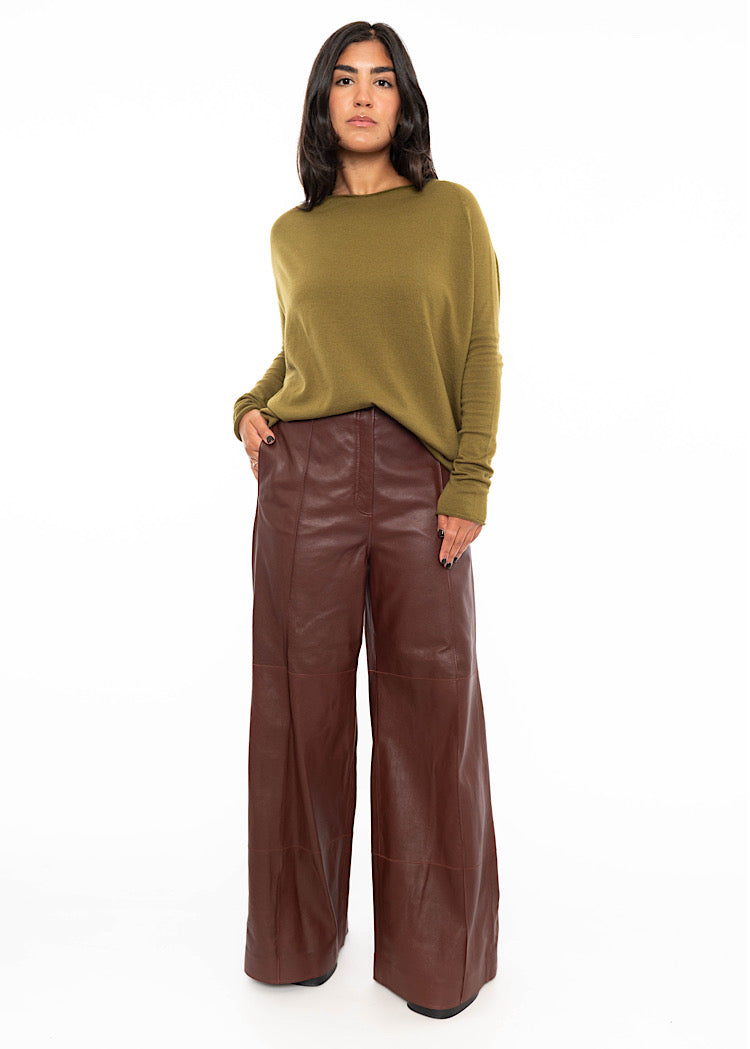 A Model wearing a relaxed fit khaki green pullover with a slash neckline and long sleeves. Styled with burgundy wide leg leather trousers.
