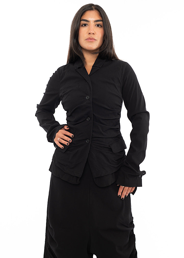 A Model wearing a minimalist techno Jacket and matching trousers, in a Black colour. Showing the fitted design.