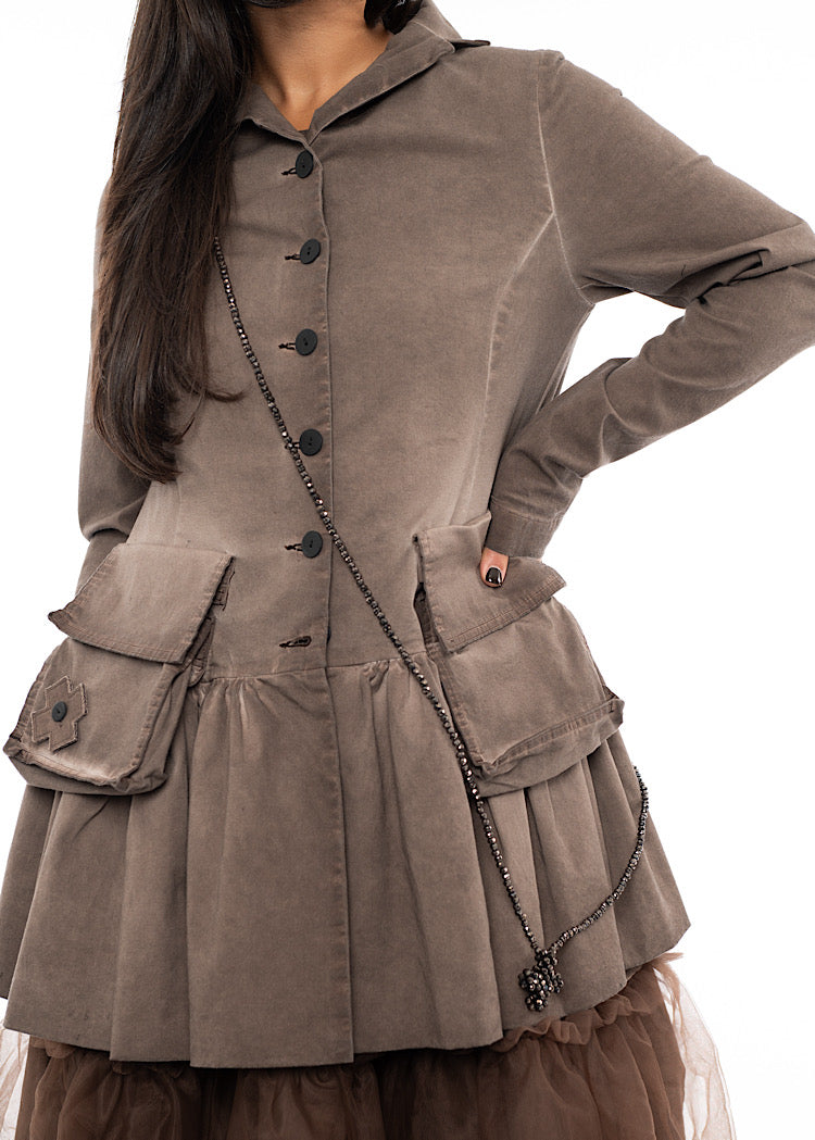 A Model wearing a long beaded necklace with a cross pendent styled with a washed Chocolate Brown Jacket and a Chocolate mesh dress.