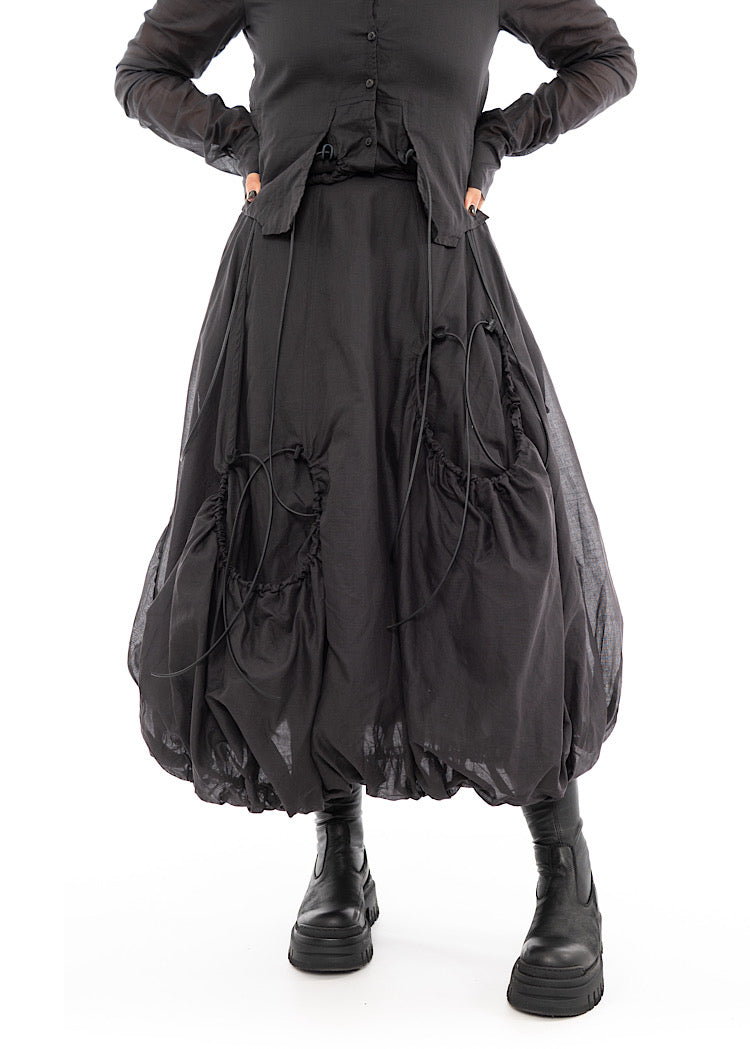 An up close photo of A Model wearing a bubble skirt, in a washed Grey colour. Focusing on the Black string details and distinct pockets.