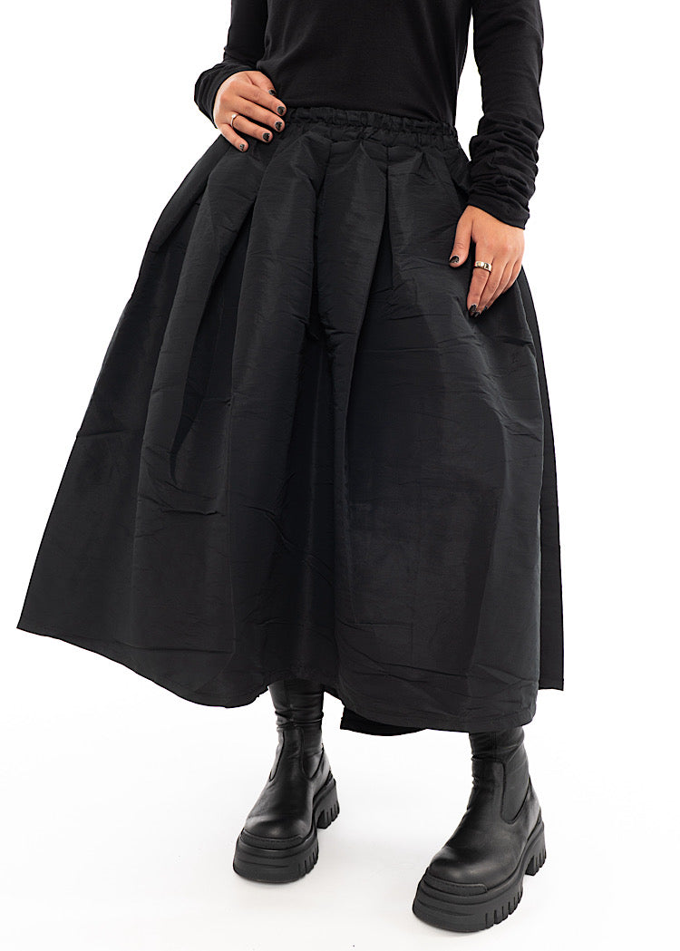 A Model wearing a Black Structured Skirt, paired with a matching Black Top and Chunky Boots. Focusing on the volume of the skirt.