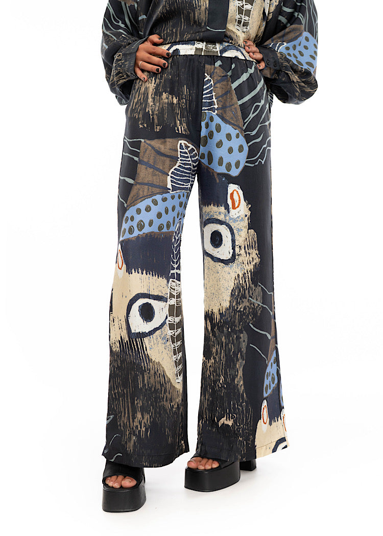 A model wearing wide leg Silk trousers with multicoloured pattern throughout. Styled with black high heels and matching silk shirt.