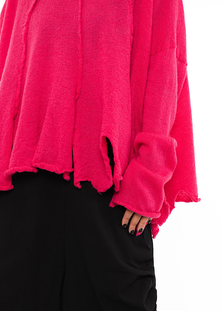 An up close of A Model standing to a side angle wearing a Bright Pink oversized Pullover. Showing the pieces texture and styled material up close.