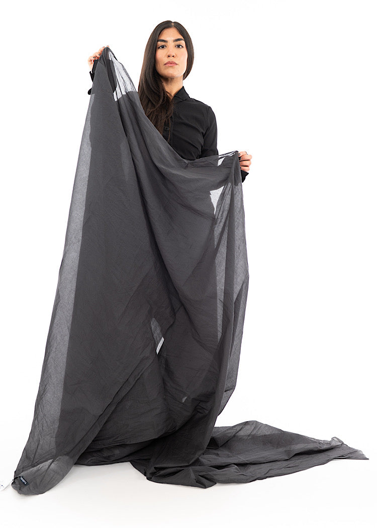 A Model holding up an oversized, washed out Grey Scarf. Showing the full length of the piece.