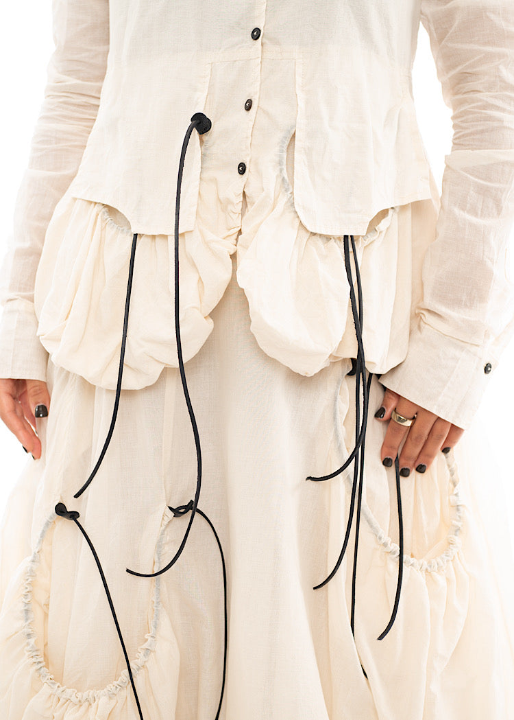 An up close off A Model wearing a sculptural Jacket with a Skirt in the matching light beige colour. Focusing on the quilted hem of the Jacket.