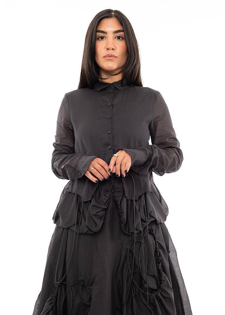 A Model wearing a sculptural Jacket with a matching Skirt in the same washed Grey colour. Focusing mainly on the cuffs.