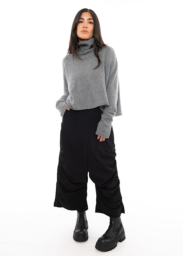 A full frame photo of A Model wearing a Grey Pullover, with a turtle neck and a straight fitted jumper. Paired with a Black Trouser and Black Boot.