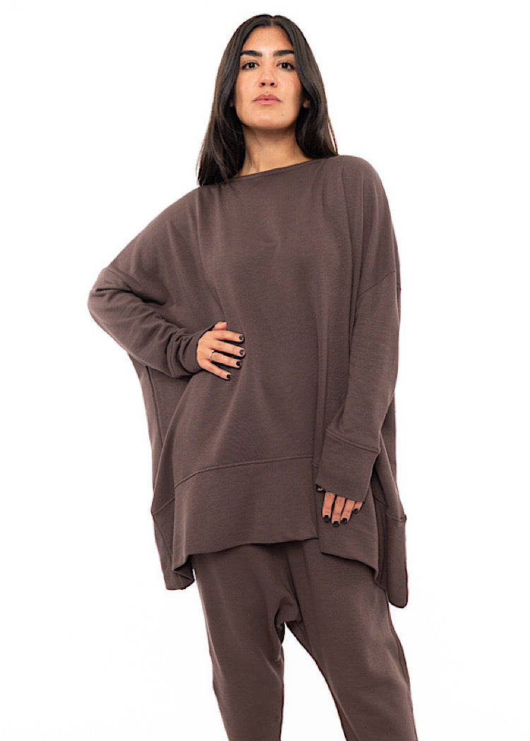 A Model wearing an oversized Plum toned Pullover, paired with a Matching Trouser. Showing the pieces long length of arm and body.
