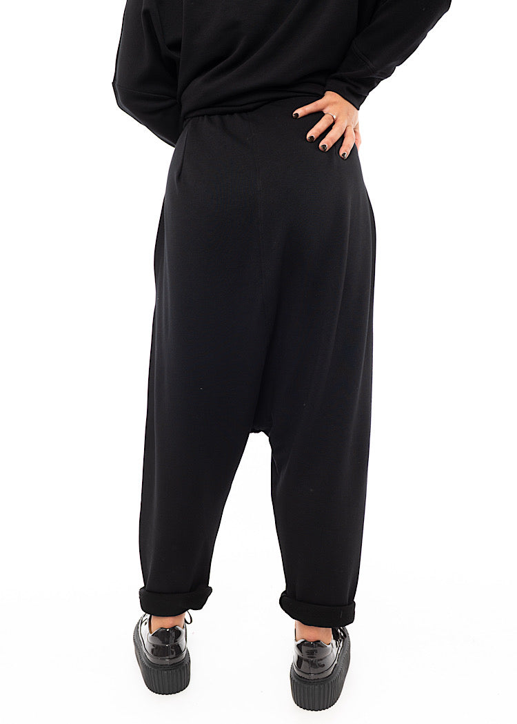 A Model standing facing the back wearing a Black fitted Trouser with a semi rolled up ankle. Showing the Trousers fit.