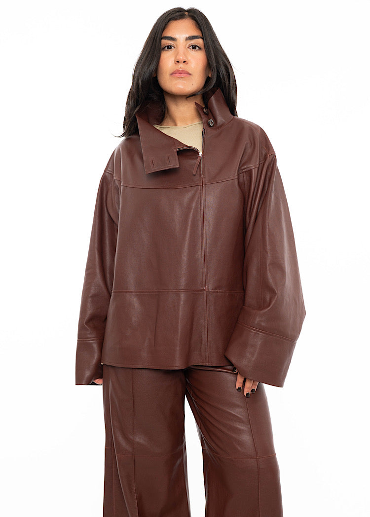 A model wearing an oversized Burgundy Leather pullover with relaxed fit sleeves with a beige pullover underneath. Styled with wide leg trousers in the matching Burgundy leather.