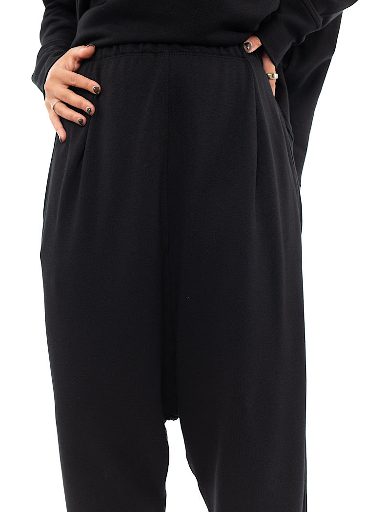 An up close off A Model standing to a side wearing a Black fitted Trouser with a semi rolled up ankle. Showing the Trousers fit.