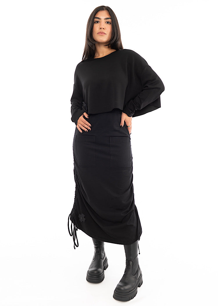 A full frame photo of A Model wearing a Black drawstring Skirt, styled with a cropped Black Pullover and Chunky Black Boot.