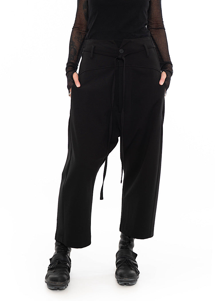 Model wearing black drop-crotch trousers with wide leg and drawstring detail, styled with mesh-sleeve top.