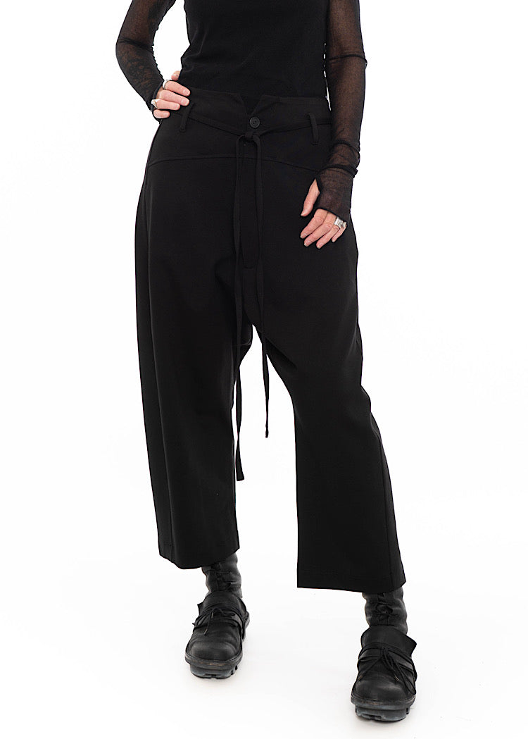 Model wearing black drop-crotch trousers with wide leg and drawstring detail, styled with mesh-sleeve top and combat boots.
