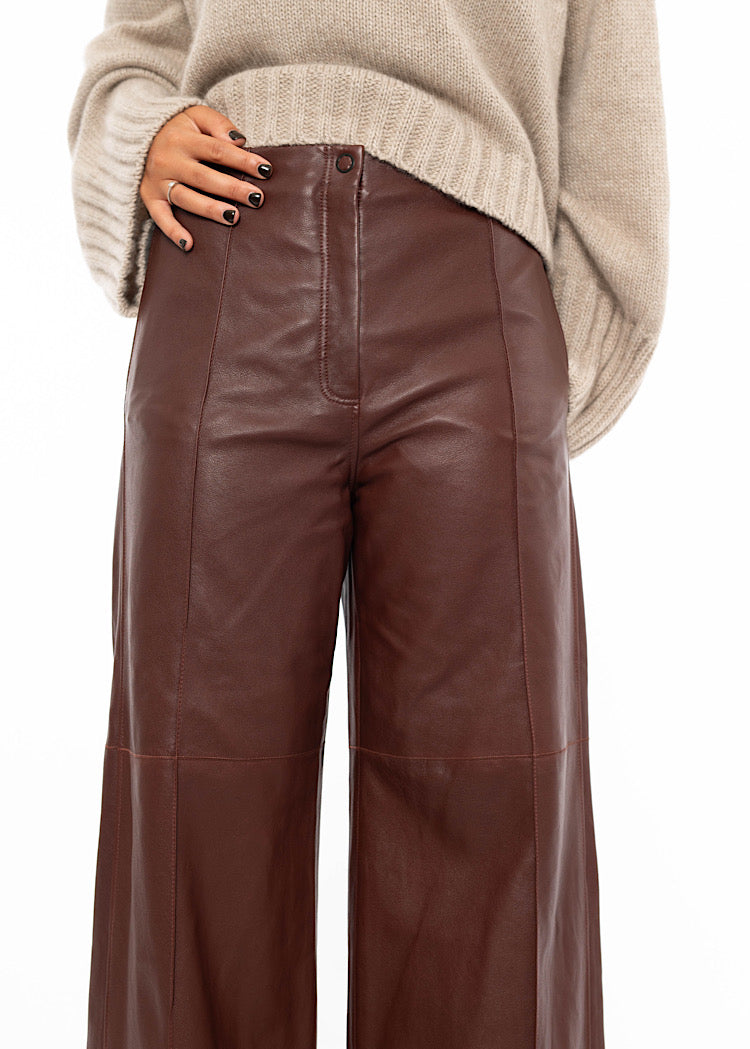 An up close of a Model wearing Burgundy wide leg leather trousers showing the minimal button which is used to fasten.