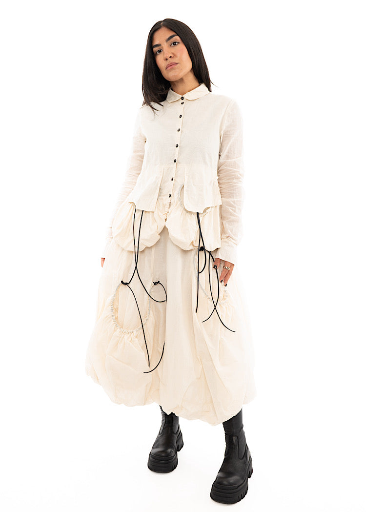 A full frame photo of a Model wearing a sculptural Jacket with a Skirt in the matching light beige colour. Focusing on the full outfit.