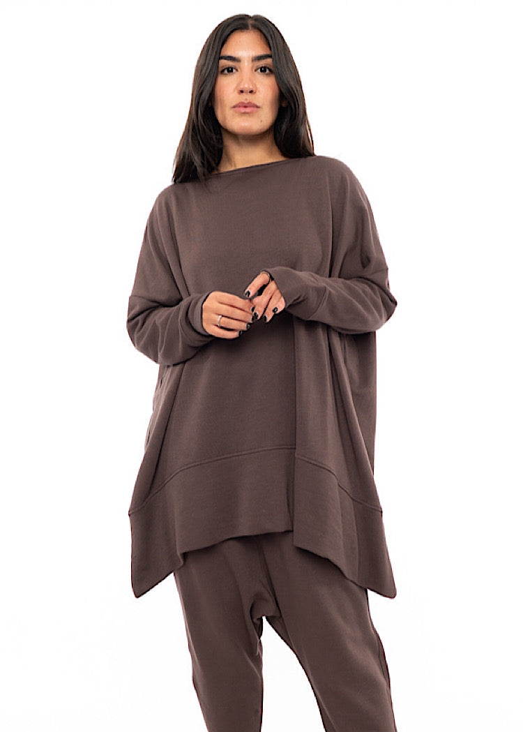 A Model wearing a comfy oversized Plum toned Pullover, paired with a Matching Trouser. Showing the pieces long length of arm and body.