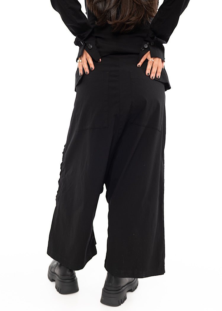 A Model standing facing the back wearing a drop-crotch Trouser in a Black colour. With a kick-flare leg and ruched side seams.