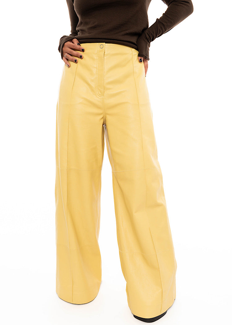 Model wearing Yellow wide leg leather trousers with a brown fitted pullover. Styled with black high heels.