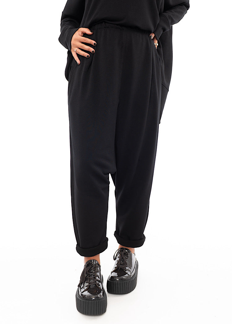 A Model wearing a Black fitted Trouser with a semi rolled up ankle. Featuring slight seam details along the elasticised waistband.