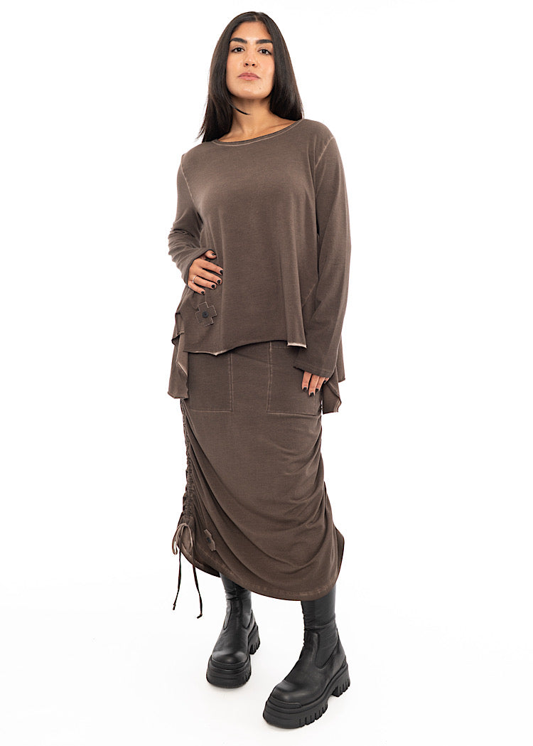 A Model wearing a Chocolate Brown skirt with distinctive details. Styled with matching Chocolate Brown pullover with layered extra material and a Black boot.