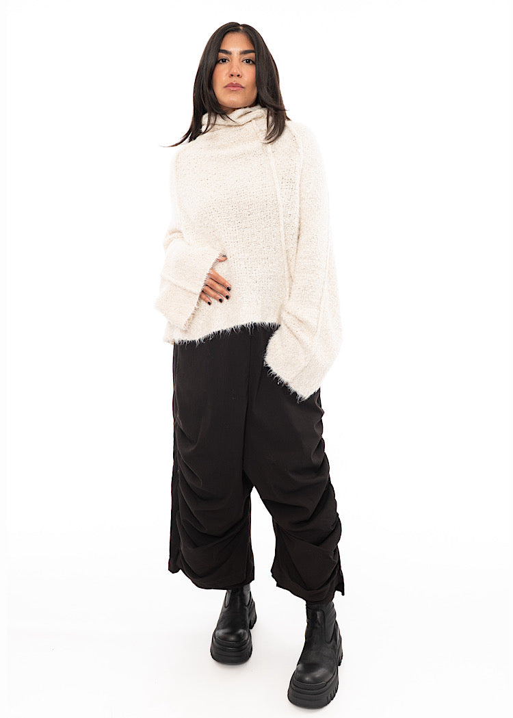 A full size photo of A Model wearing a Light creme, Fluffy pullover featuring a turtle neck feature and an oversized fit. Paired with Black trousers and Black Boot.