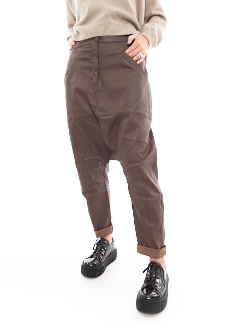 A Model wearing a Structured Drop-Crotch Brown Leather Trouser. Showing the curved seam-lines throughout the Trouser.