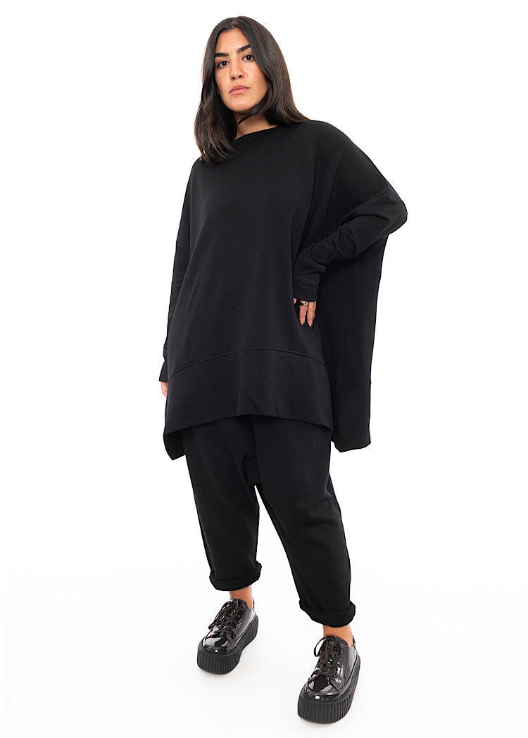 A Full frame photo of A Model wearing a Black fitted Trouser.Styled with a matching pullover and patent Shoe.