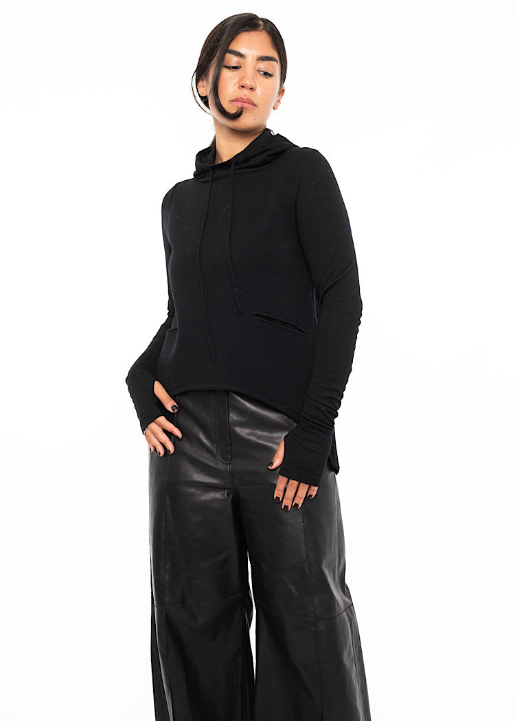 A model wearing a fitted black pullover with a drawstring high neckline, an asymmetric hemline, distinct whole thumbs and an added minimal pocket detail.