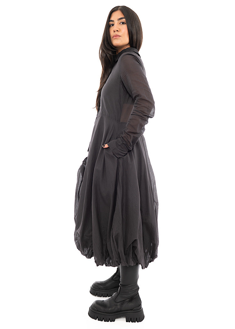 A Model standing to the side wearing a bubble skirted Dress in a washed Grey colour. Focusing on the width and fit of the piece.
