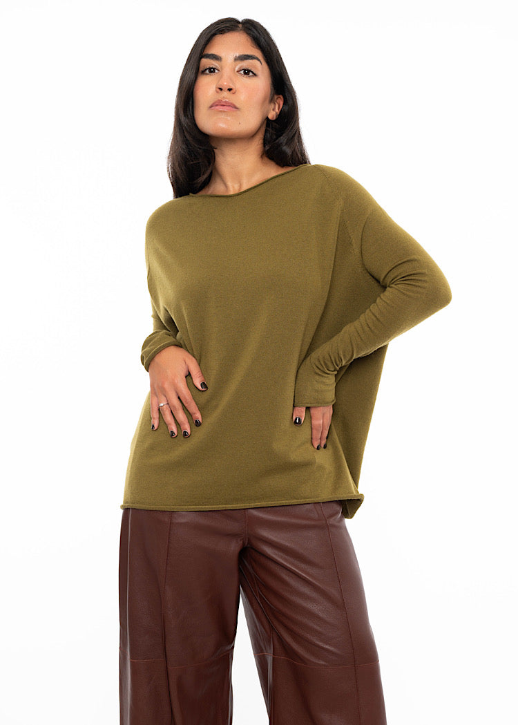 A Model wearing a relaxed fit khaki green pullover with a slash neckline and long sleeves. Showing the fitted areas of the pullover and the more relaxed areas .
