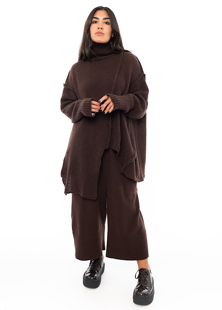 A Full frame photo of A Model wearing a Brown Oversized pullover featuring grungy pieces of fabric. Showing the ribbed cuffs in more depth.
