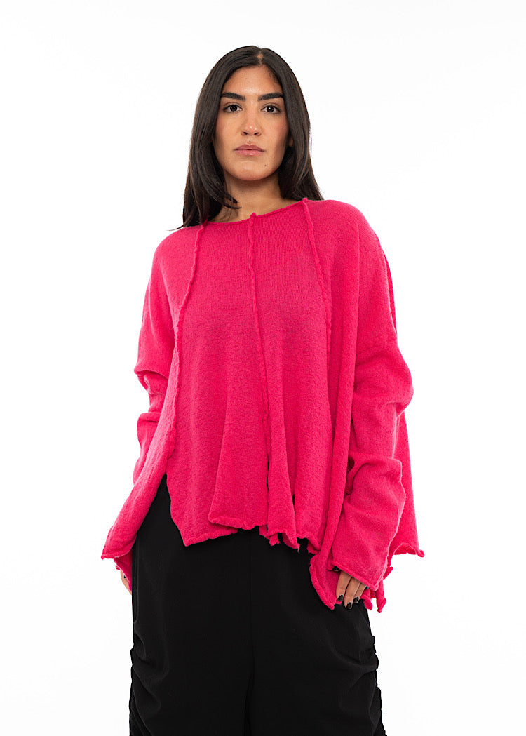A Model wearing a Bright Pink oversized Pullover. Featuring distinct seam-lines and a cut out like hem line.