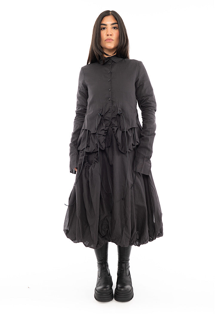 A full frame photo of A Model wearing a sculptural Jacket with a matching Skirt in the same washed Grey colour. Paired with a Black Chunky Boot.