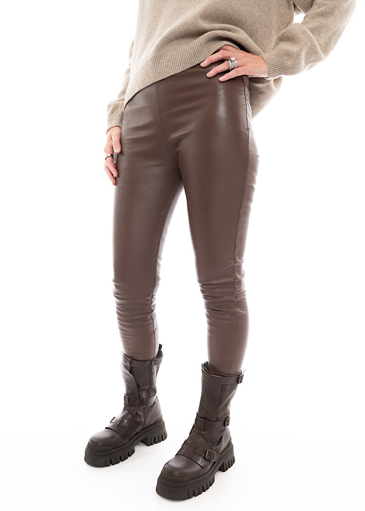 A Model wearing a tight fitting Legging-Like Chocolate Leather Trouser, paired with a grungy style boot and creme coloured pullover.