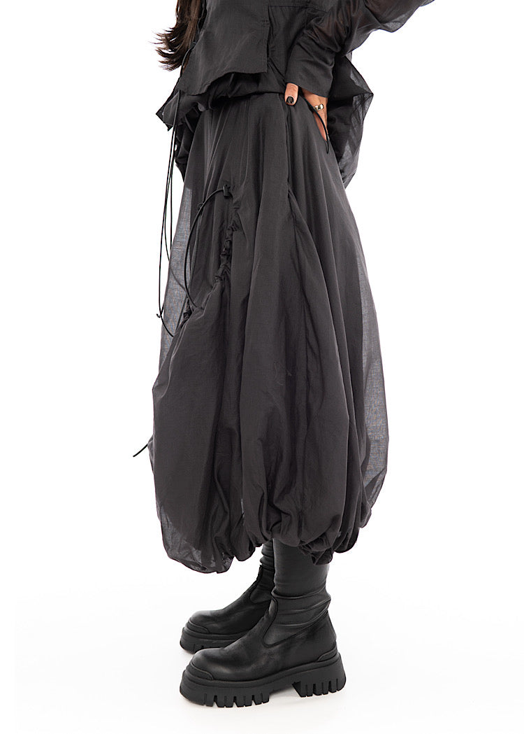 A Model standing to the side wearing a bubble skirt, in a washed Grey colour. Showing the Skirts width and volume.