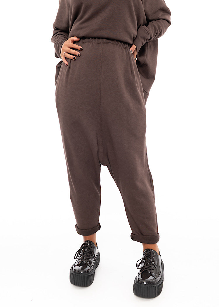 A Model wearing a plum toned drop-crotch trouser with a slight rolled up effect on the Ankle. Paired with matching pullover and patent shoes.