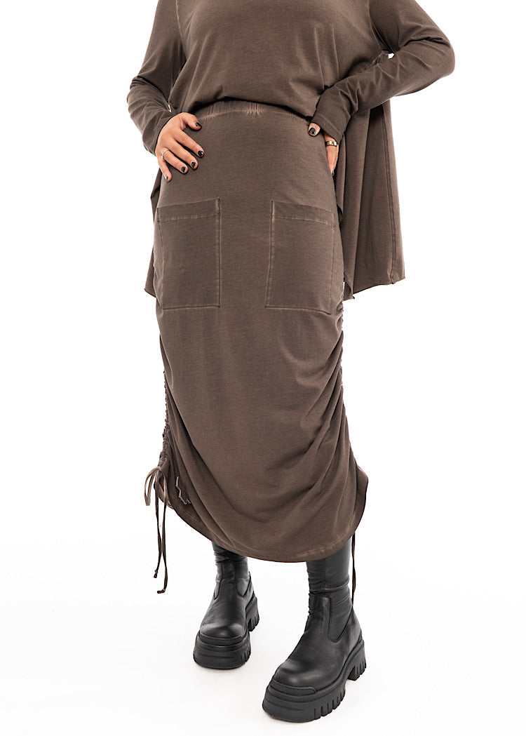 A Model wearing a Chocolate Brown skirt with distinctive details. Styled with matching Chocolate Brown pullover with layered extra material and a Black Chunky boot.