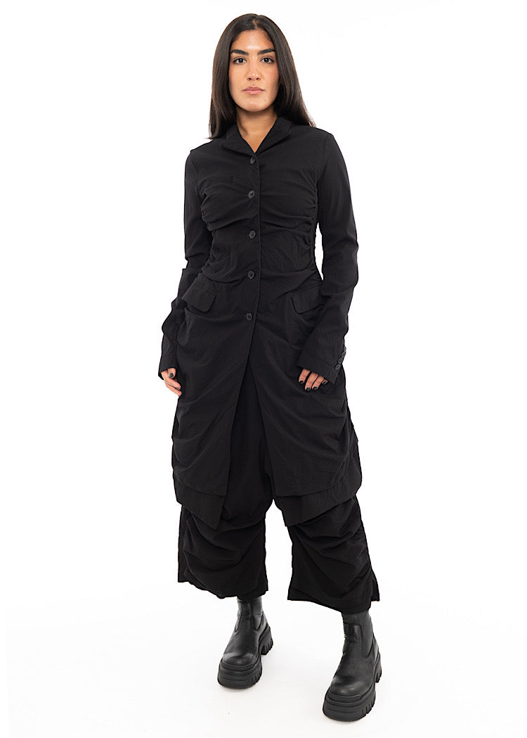 A full frame photo of A Model wearing a detailed techno coat and matching trousers, in a Black colour. Paired with a chunky Boot.