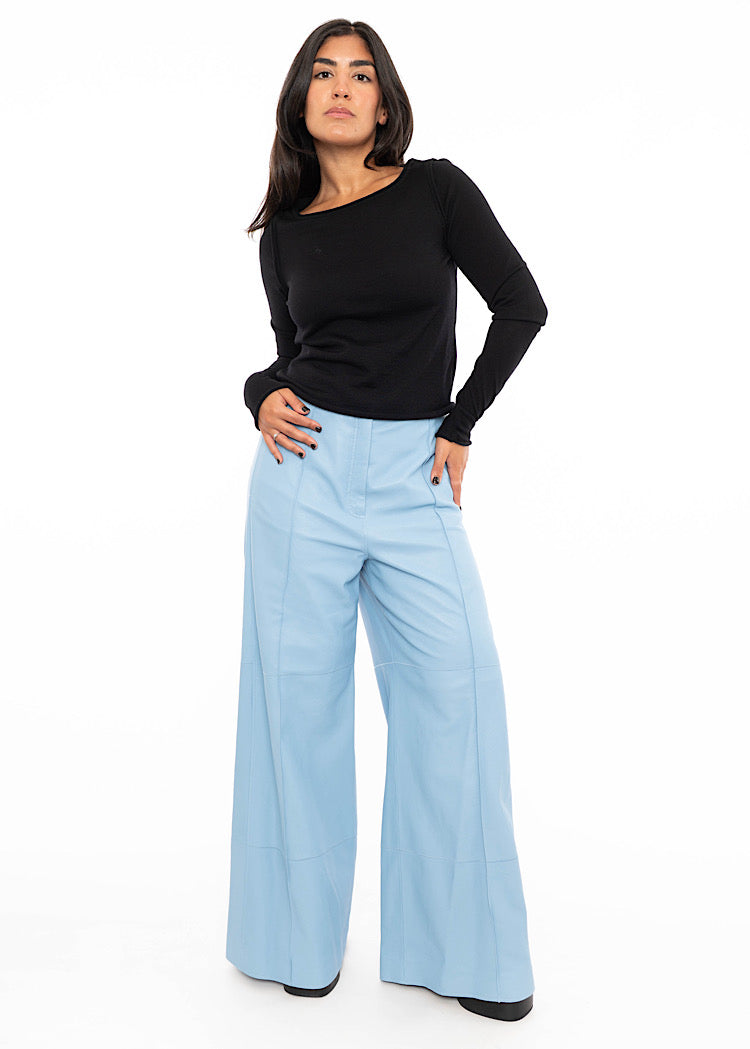 Model wearing light blue wide leg leather trousers with a seam detail down the centre of the leg. Styled with a fitted black pullover and black high heels.