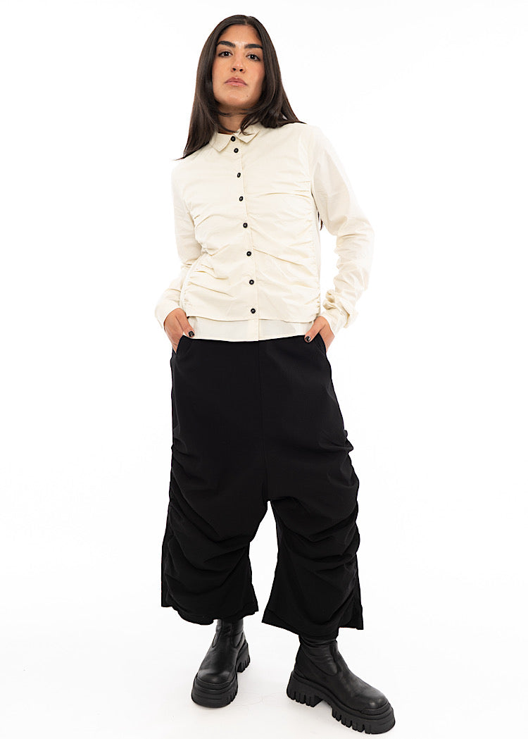 A full frame photo of A Model wearing a fitted ruched buttoned up Shirt, paired with a pair of Black trousers and Chunky Black Boots.