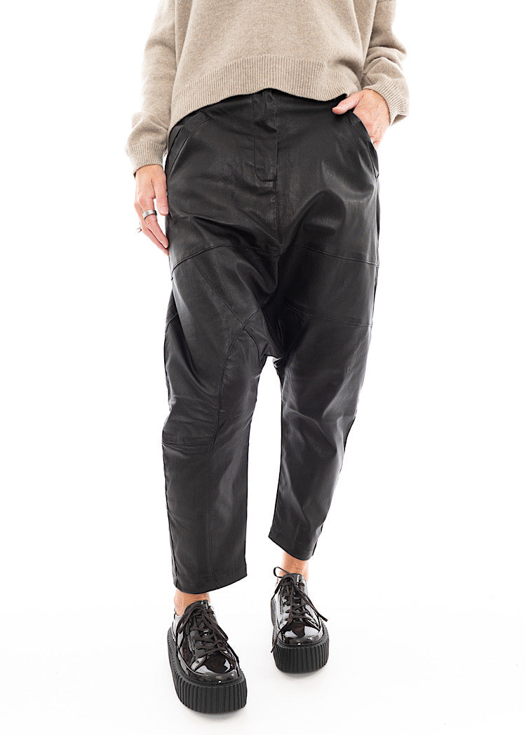A Model wearing a Structured Drop-Crotch Black Leather Trouser, disclosing the pockets. Showing the seam-lines in more detail.