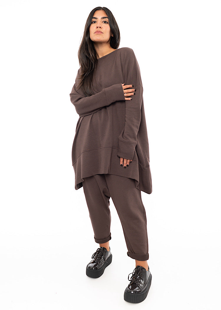 A full frame photo of A Model wearing a plum toned drop-crotch trouser. Paired with matching pullover and patent shoes.