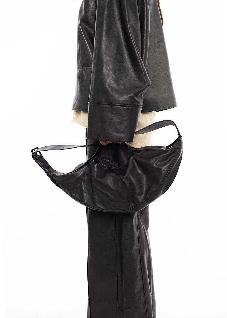 Close up of Model wearing a black Leather jacket, with a matching trouser. Holding Black Slouchy leather bag on a shorter strap which blends into the colour and style of other leather pieces.