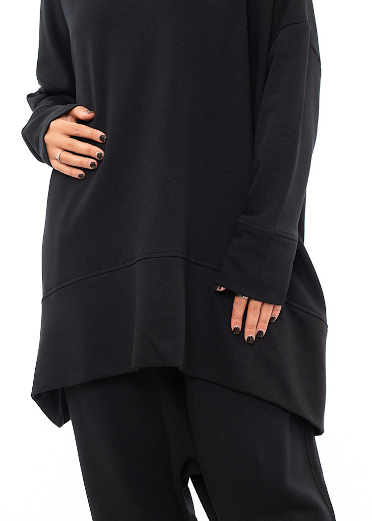 An up close off A Model standing to a side wearing a Black Oversized Pullover. Showing the length of the Arm.