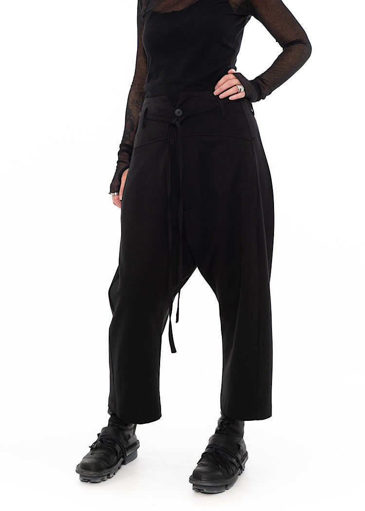 Model wearing black drop-crotch trousers with wide leg and drawstring detail, styled with mesh-sleeve top and combat boots.