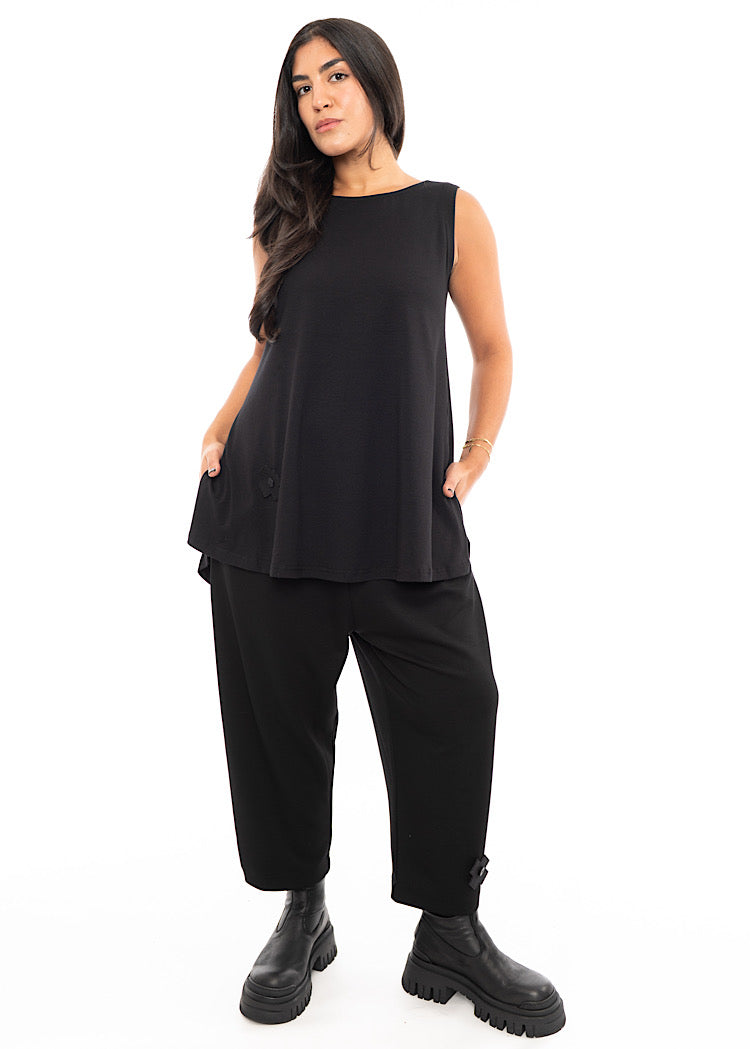 A Model wearing a fitted Black Top with slits up the side, sleeveless design and rounded neckline. Styled with Black Trouser and Chunky Black Boot.